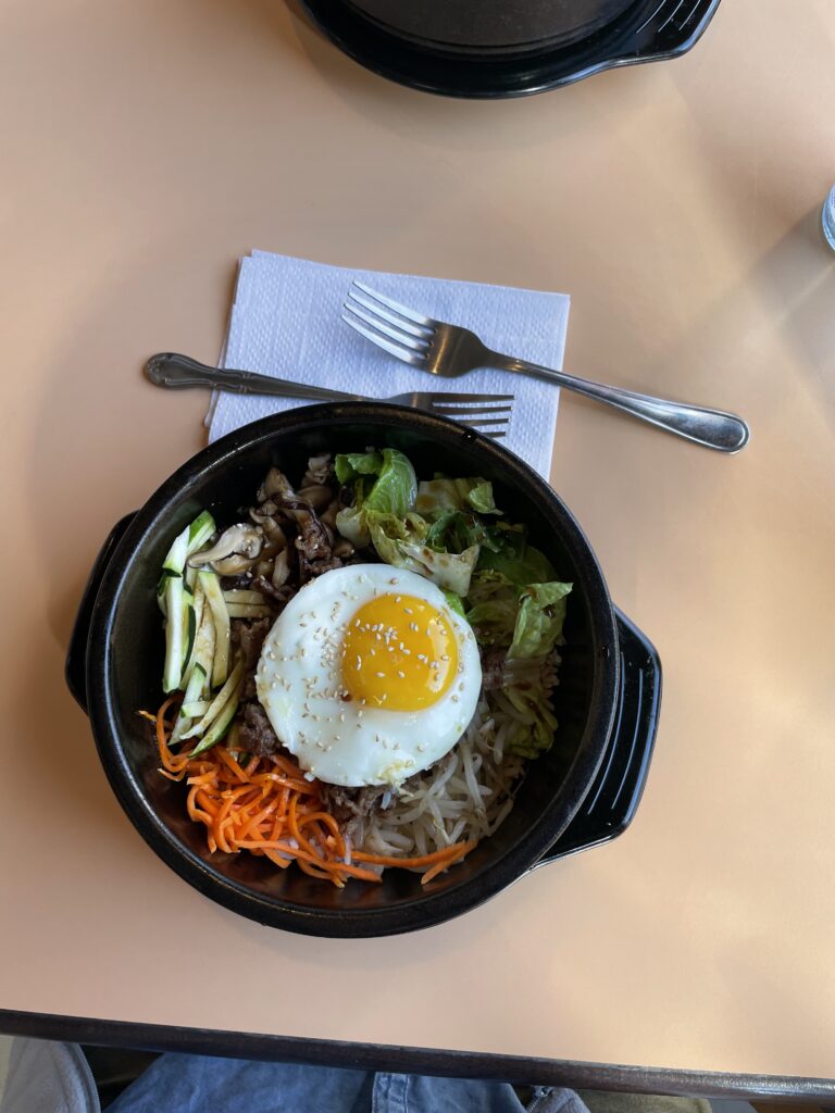 Bibimbap with a runny egg on. Also on the table are two forks and a napkin.