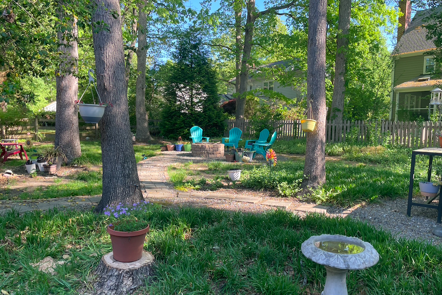 Backyard garden with walking path, trees, flowers, bird bath, and fire-it seating