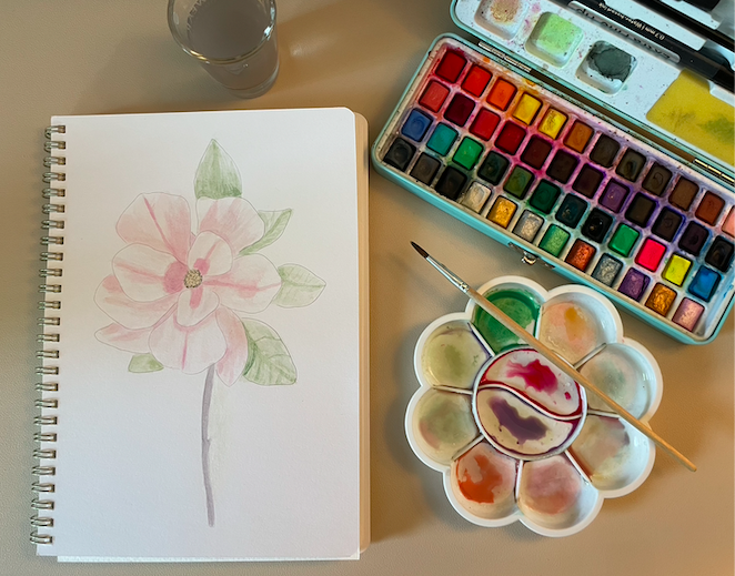 Watercolor image of a pink flower with watercolor paints, color mixer, water cup, and brush